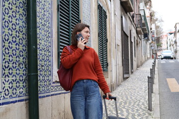 Fototapeta premium A woman with a suitcase walks along the cobblestones of the old town and talks on the phone