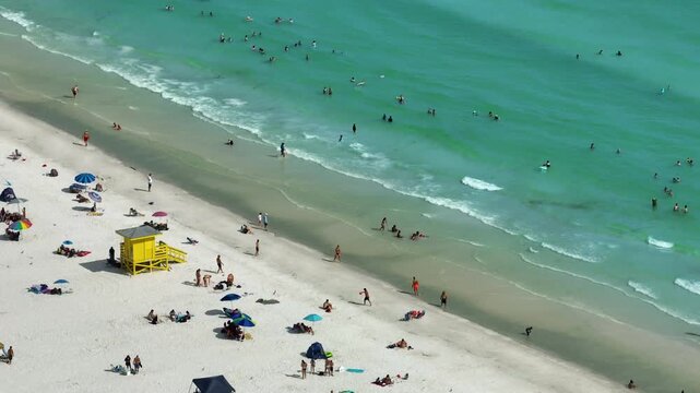 Siesta Key sandy beach in Sarasota, USA. Many tourists enjoying summer vacation time swimming in warm Mexico gulf water and sunbathing on hot Florida sun.