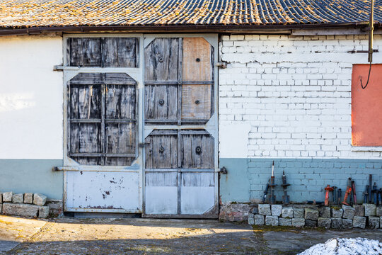 Old wooden barn doors on brick wall with tiled roof in rural yard