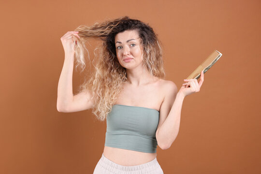 Unhappy woman trying to brush her tangled hair on brown background