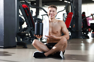 Obraz premium Happy young man with jar of protein powder in gym
