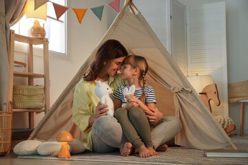 Mother and her daughter with toys near wigwam at home © New Africa