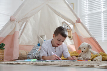Little boy drawing in sketchbook near toy wigwam at home © New Africa