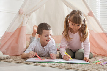 Little kids drawing in sketchbook together near toy wigwam at home © New Africa