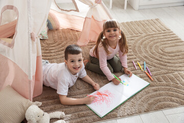 Little kids drawing in sketchbook together near toy wigwam at home, above view © New Africa