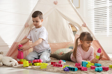 Little kids playing with building blocks near toy wigwam at home © New Africa