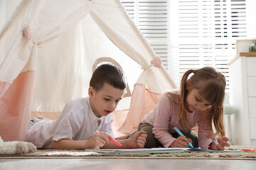 Little kids drawing in sketchbook together near toy wigwam at home © New Africa
