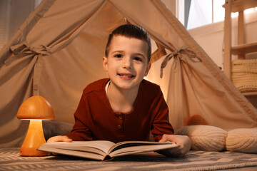 Little boy reading book near toy wigwam at home © New Africa