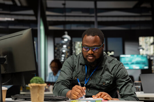 Male consultant engaged in handwriting notes for monthly reports, extracting essential highlights from finance documents and making a summary for business goals and upcoming tasks.