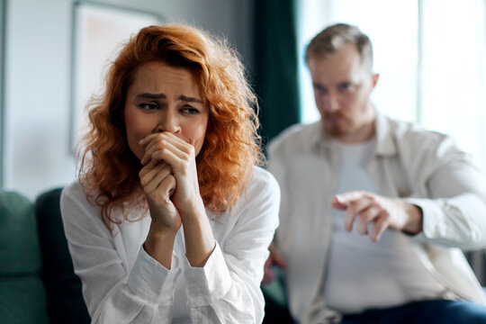 Angry emotional man shouting at his depressed crying wife, couple having quarrel at home. Domestic abuse concept