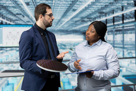 Man and coworker overseeing silicon wafers manufacturing operations in high tech factory. Managers doing industry 4.0 automation integration in semiconductor substrates manufacturing plant