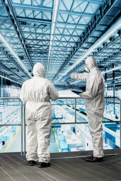 Engineering team optimizing microchip smart factory supply chain logistics, wearing bunny suits. Technicians in safety gear monitoring industry 4.0 semiconductor manufacturing plant systems