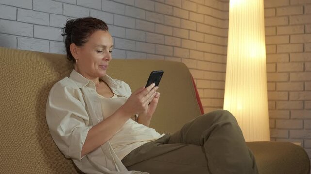 Problem of technology dependence. Mature woman sitting on the couch using her smartphone when her husband asks her to put it away