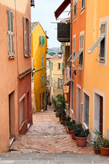 Fototapeta premium Charming narrow street with colorful houses and shutters in Villefranche-sur-Mer, France. Traditional Mediterranean architecture with warm tones and cozy travel atmosphere.