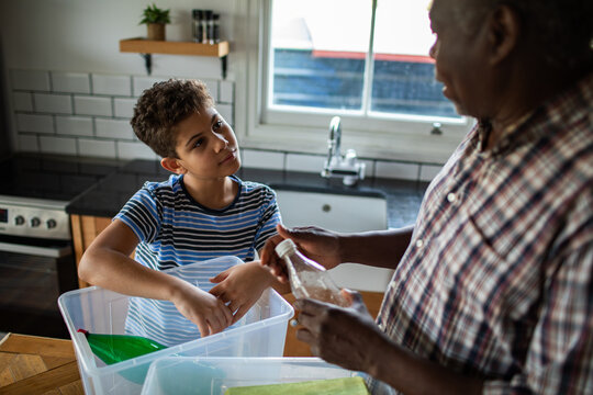 Older man teaching boy to recycle in home kitchen