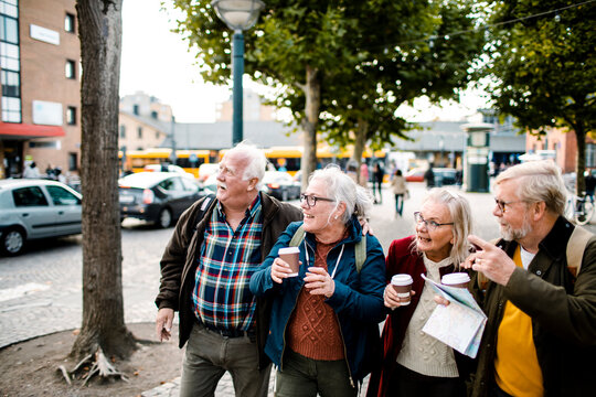 Four senior friends sightseeing with coffee on city street