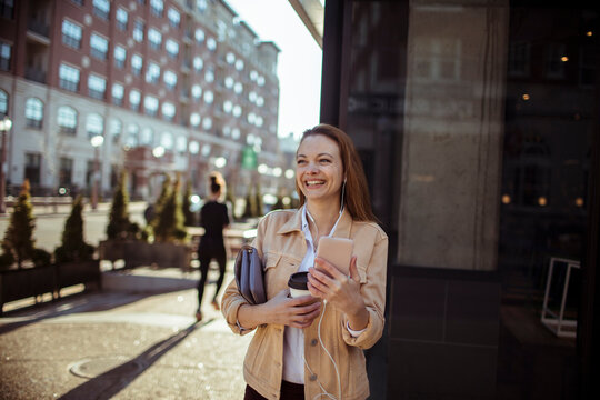 Smiling young woman with smartphone and coffee on city street