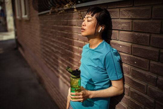 Runner resting with water bottle against urban brick wall