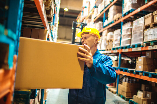 Worker in hard hat lifting box in warehouse aisle