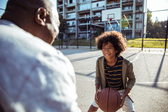 Smiling boy playing basketball with adult on outdoor urban court