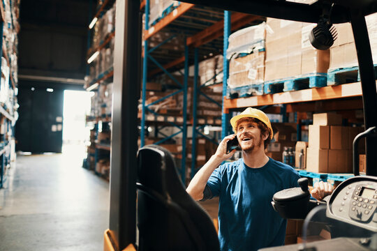 Smiling warehouse worker talking on phone by forklift in distribution center
