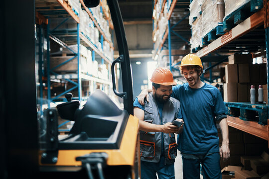 Two warehouse workers checking smartphone beside forklift