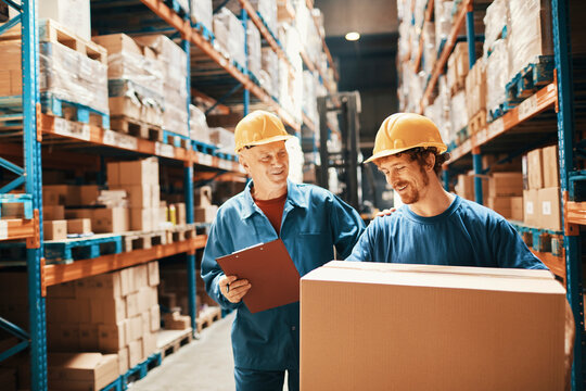 Two warehouse workers wearing hard hats checking inventory in distribution aisle