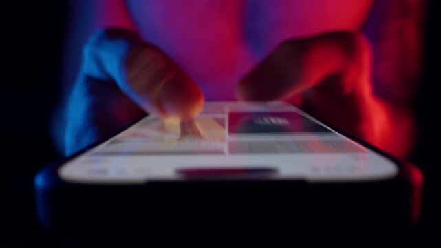 Fingers Tap Bright Screen in Dark Room with Red and Blue Light, Low Angle Close-Up Showing Constant Connectivity Reflecting the Concept of the Whole Life is in the Smartphone