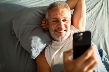 Smiling mature man video calling in bed at home