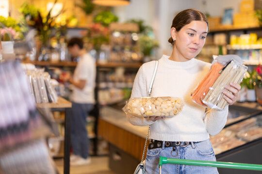 Young female shopper buying package of pasta in organic grocery store