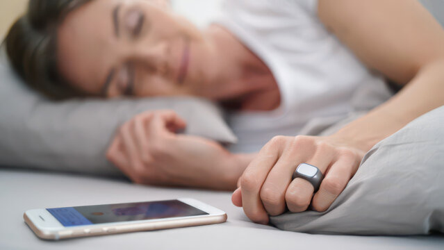 smart ring fertility tracker on woman hand during sleep, smartphone app cycle analytics bedside, ovulation monitoring wearable sensor, basal temperature night data, femtech hormonal insights