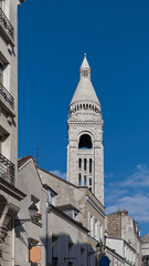 Fototapeta premium Sacre Coeur basilica tower rising above Montmartre roofs under blue spring sky