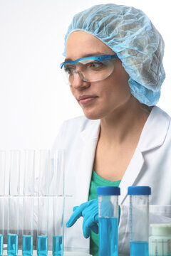 Young european female scientist in lab coat observes vials with blue liquid while wearing PPE