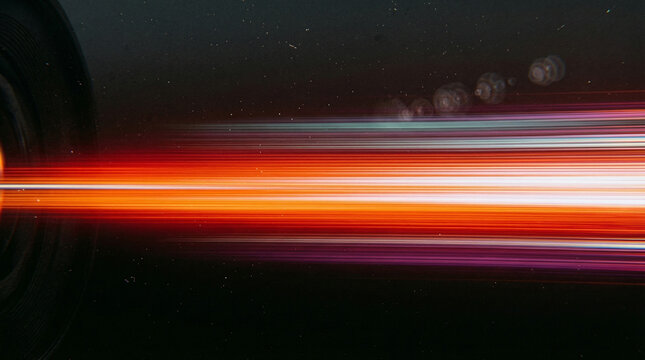 Abstract streaks of vibrant orange, red, and purple light blur horizontally across a dark, star-filled background, suggesting rapid motion or hyperspace travel.