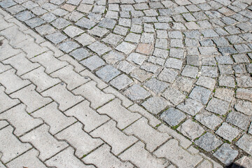 Fototapeta premium Diagonal transition between cobblestone and concrete pavement creating contrasting urban texture background with geometric structure