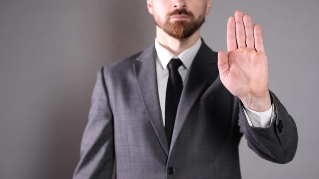 Businessman showing stop sign on grey background, closeup