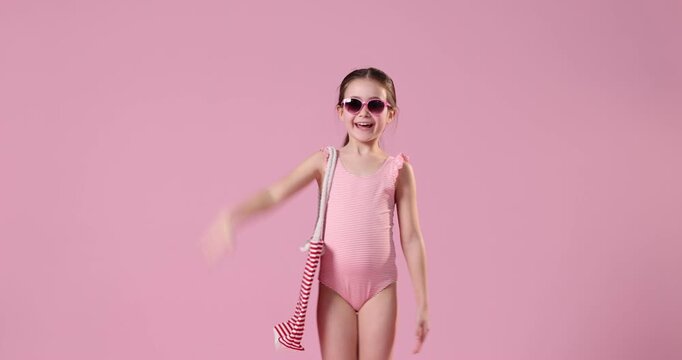 Little girl in swimsuit with beach bag on pink background