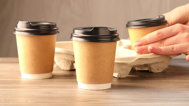 Woman putting takeaway paper cups with coffee into cardboard holder at wooden table, closeup