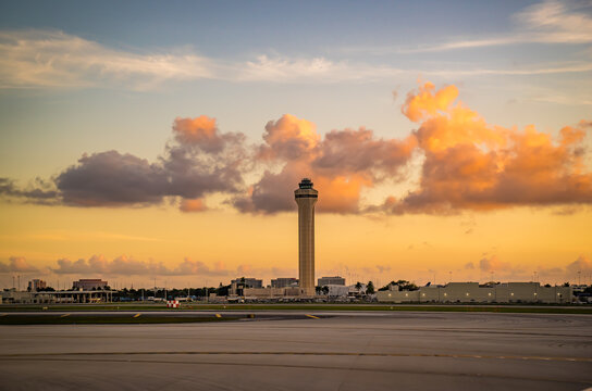 Beautiful sunset at Miami International Airport. The airport traffic air control tower is bathed in orange sunlight. The tower is surrounded by a magnificent cover of clouds
