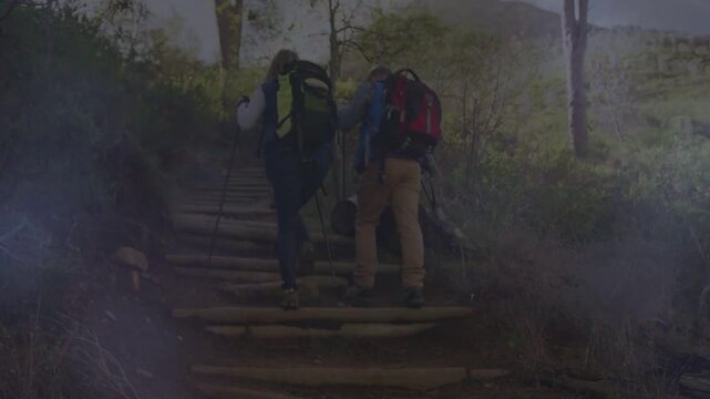 Hiking couple climbing log steps at trail start, planting pole and carrying backpacks to ridge