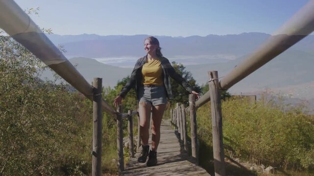 Vertical video: Walking hiker starting using rails on wood bridge over valley looking in yellow tee