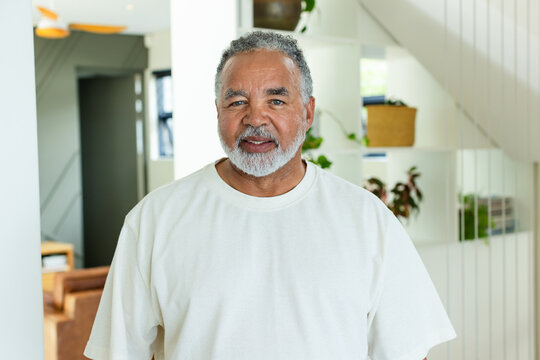Senior man standing in modern home wearing white T-shirt by built-in shelves, plants, basket