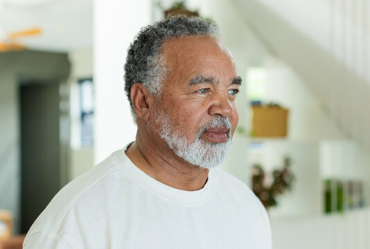 Senior African-American man standing facing right in bright room wearing white crewneck with plants