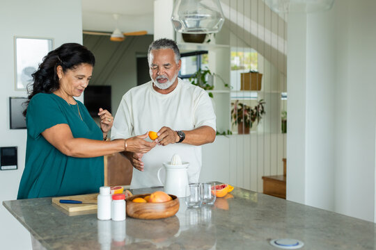 Mature couple handing citrus while juicing on stone kitchen island with electric reamer, glasses
