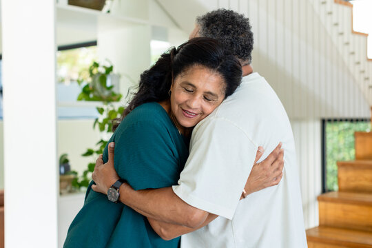African American senior couple embracing in home foyer, woman wearing teal top, wristwatch visible