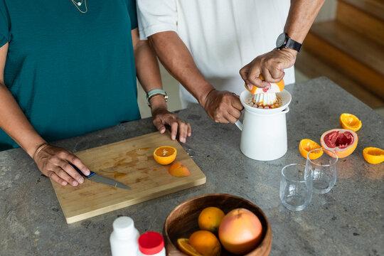 African American couple pressing juicer after halving citrus on board at kitchen counter for juice