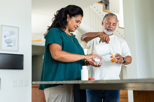 Senior couple dispensing pills from pill bottle, pouring juice from pitcher at kitchen counter