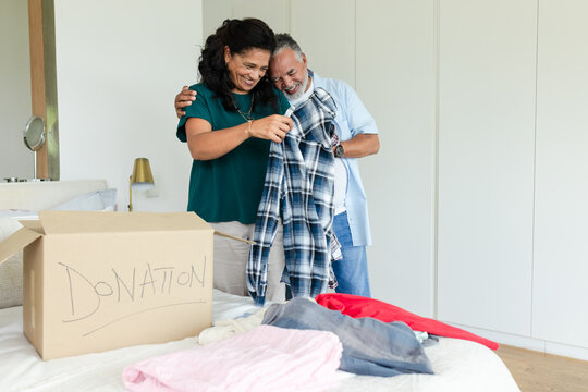 African American couple smiling, holding plaid shirt, sorting clothes into DONATION box in bedroom