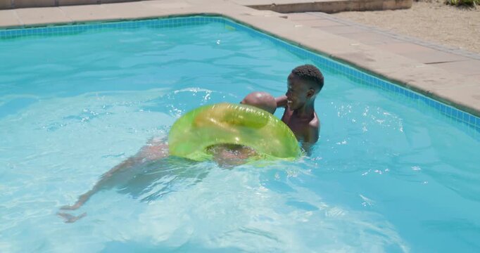 African father and son playing in backyard pool, son pushing father onto green ring, then falling