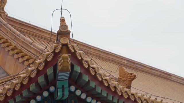 Golden temple roof finial closeup, ornate guardian figure perched on eave, glazed tiles under muted sky, aerial framing evokes reverence and craftsmanship, versatile for heritage storytelling